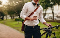 Businessman holding a coffee cup and walking to office taking his bicycle with him
