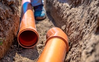 Close up of laying drainage pipes into the ground. Drainpipes are orange and sit in a soil trench.