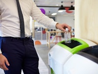 Man in an office recycling plastic bottle close up of hand as he puts the bottle in the lime green recycling bin