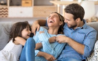 Cheerful family sitting on couch in living room have fun little daughter tickling mother laughing