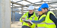 Engineer working on building site with two apprentices reviewing some plans wearing hard hats and high-vis vests