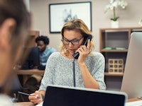 Mature businesswoman wearing glasses talking on landline phone in office.