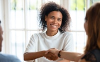 Smiling female office staff shaking hand of client at meeting
