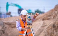 Surveyor engineer wearing safety uniform and helmet with equipment theodolite to measurement positioning on the construction site of the road with construct machinery background.